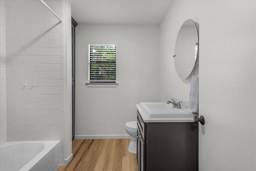 Bathroom featuring a single vanity with dark cabinetry, integrated sink, and round wall-mounted mirror