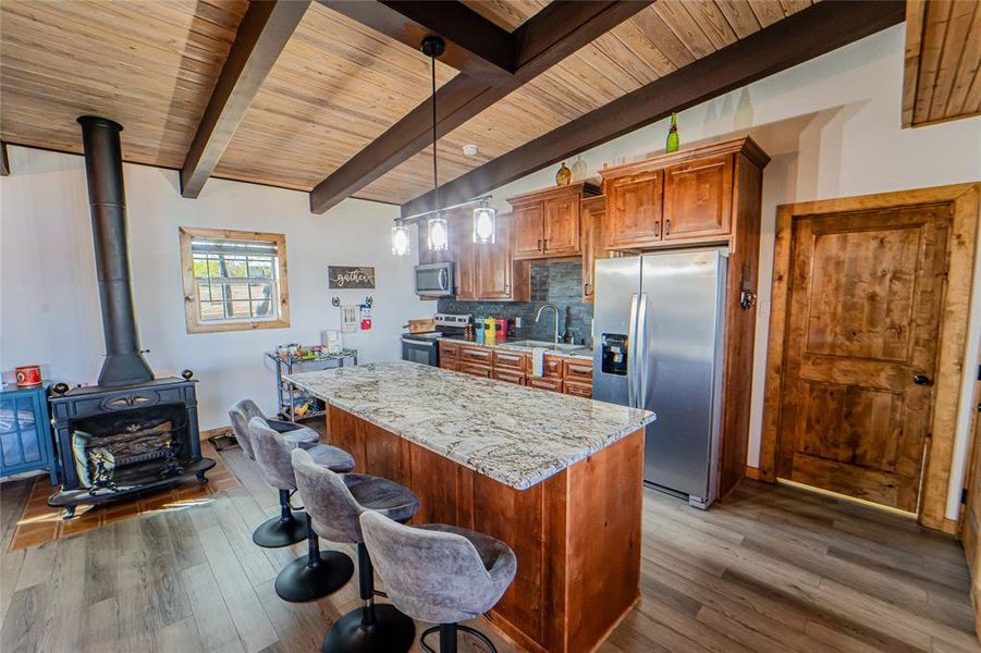 Updated kitchen with oversized island seating-Kitchen featuring wood finish cabinetry, stainless steel appliances, neutral flooring, a center island, and lofted ceiling with beams Updated kitchen with oversized island seating-Kitchen featuring wood finish cabinetry, stainless steel appliances, neutral flooring, a center island, and lofted ceiling with beams