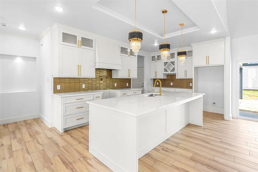 Kitchen featuring ornamental molding, light stone countertops, light wood-type flooring, white cabinets, and an island with sink