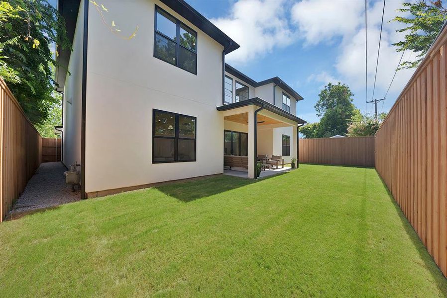 Expansive rear yard featuring a manicured lawn, a covered patio with a ceiling fan, and full privacy fencing