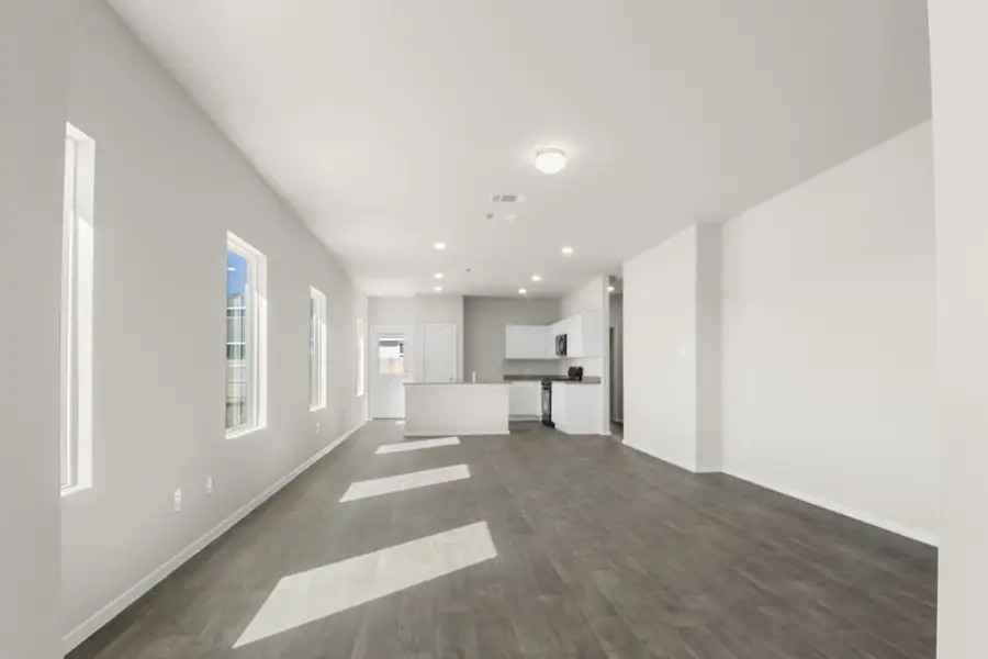 Image of a living room with cream walls, dark brown floors and an open kitchen in the distance