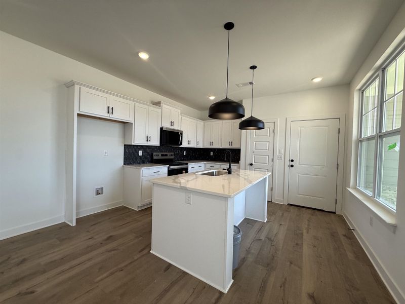 Kitchen featuring white cabinetry, stainless steel appliances, a center island with sink, decorative backsplash, and light stone counters