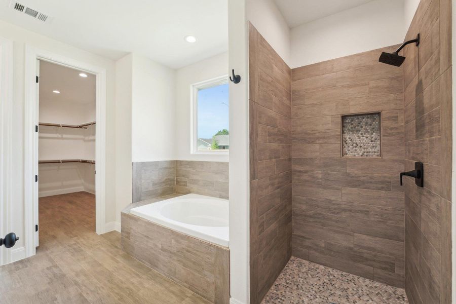 Full bath with a garden tub, wood tile floors, a stall shower, a spacious closet, and visible vents Full bath with a garden tub, wood tile floors, a stall shower, a spacious closet, and visible vents