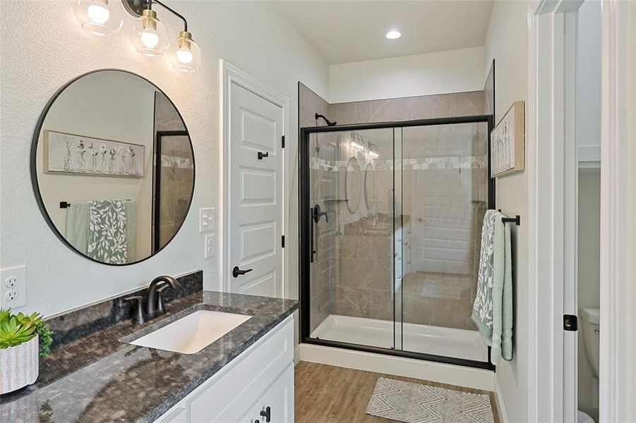Contemporary bathroom featuring a single vanity with a dark granite countertop, a rectangular undermount sink, and a circular mirror