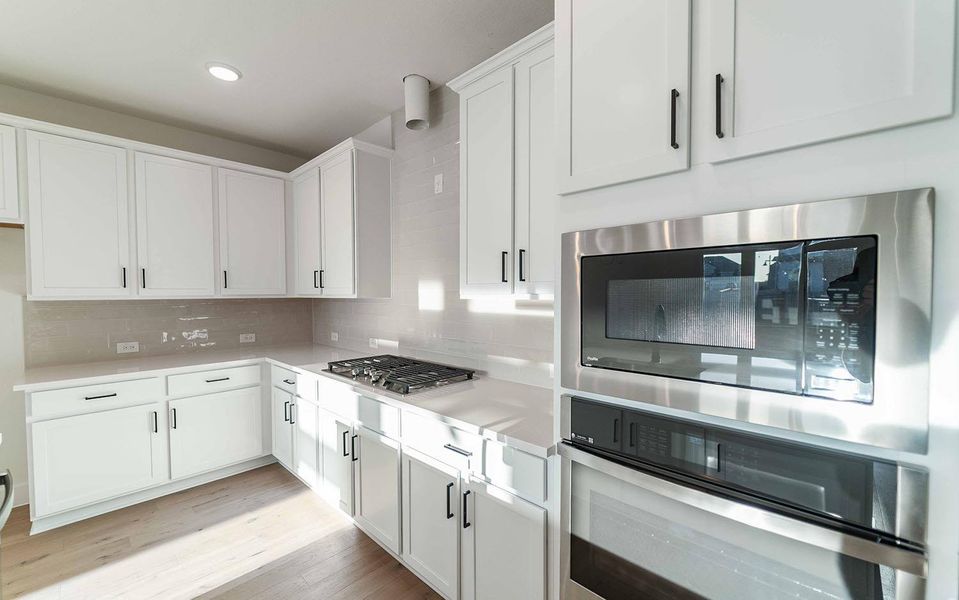Kitchen featuring appliances with stainless steel finishes, light countertops, tasteful backsplash, white cabinetry, and light wood-style floors