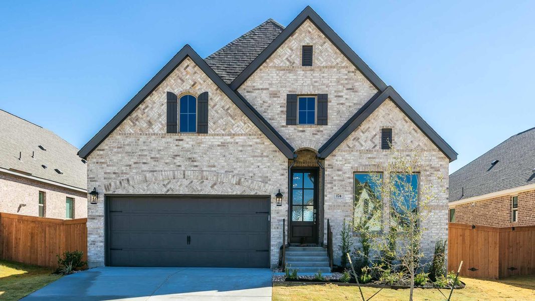 French country home with concrete driveway, a garage, fence, and brick siding