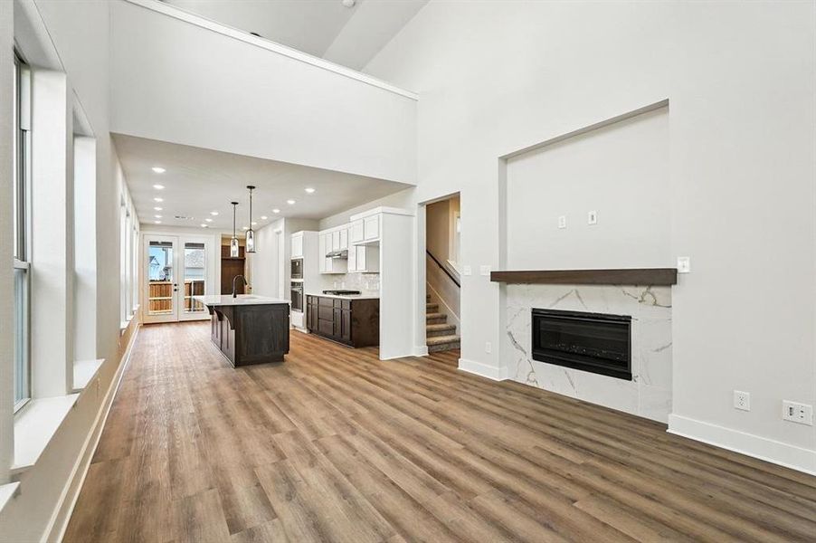 Unfurnished living room featuring recessed lighting, a fireplace, light wood-type flooring, a high ceiling, and stairs Unfurnished living room featuring recessed lighting, a fireplace, light wood-type flooring, a high ceiling, and stairs