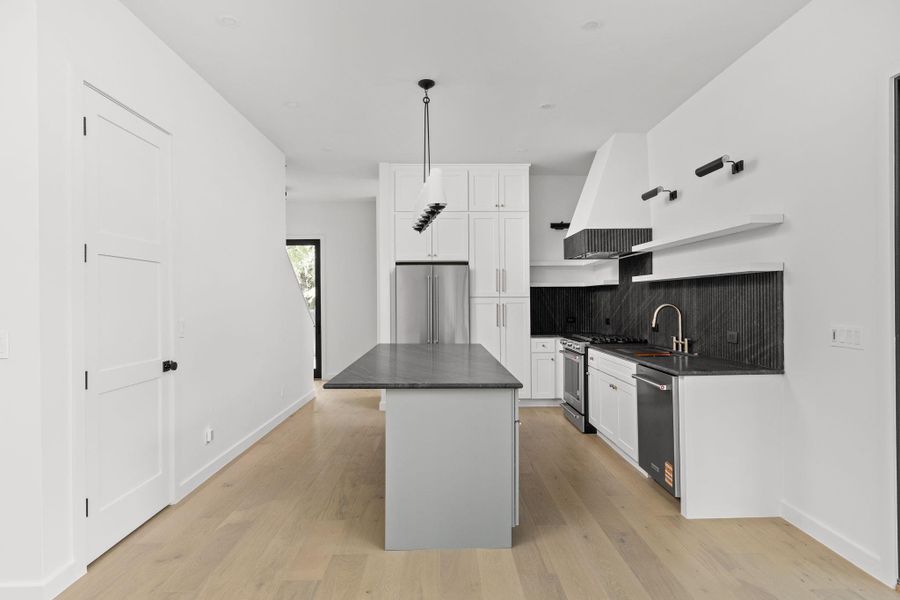 Kitchen featuring high quality appliances, dark countertops, premium range hood, and backsplash