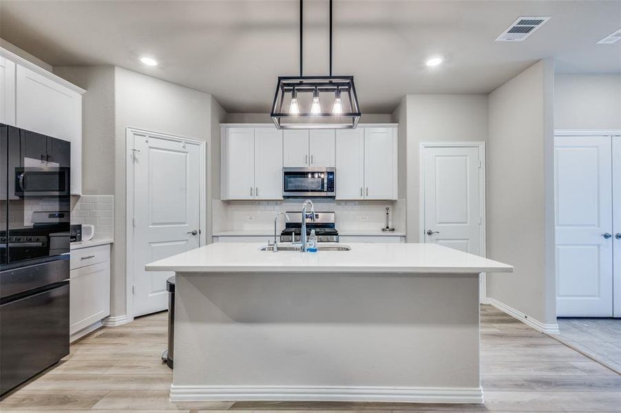 Kitchen with stainless steel appliances, an island with sink, white cabinetry, pendant lighting, and tasteful backsplash