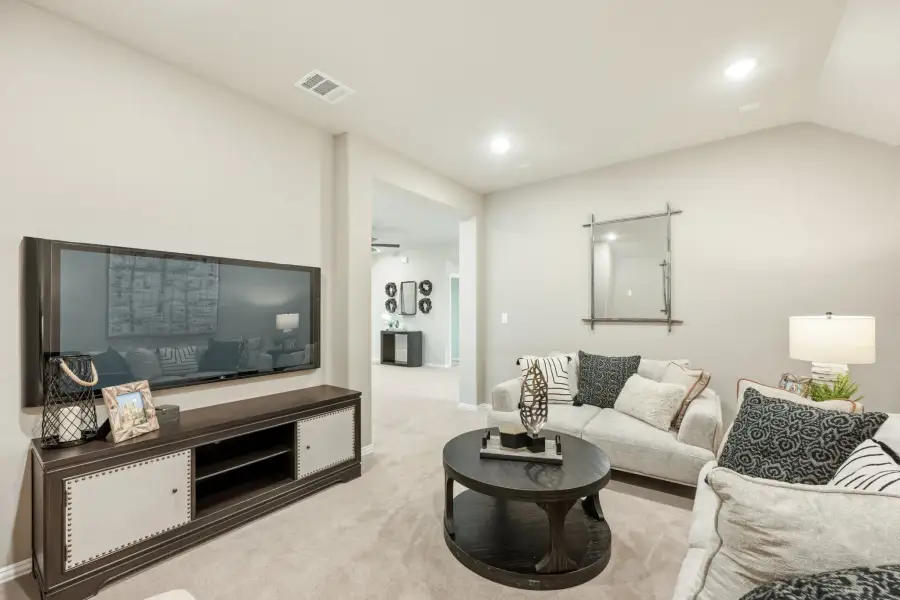 Living room with wall-mounted TV, dark wood media console, white sofa, and round coffee table on light carpet