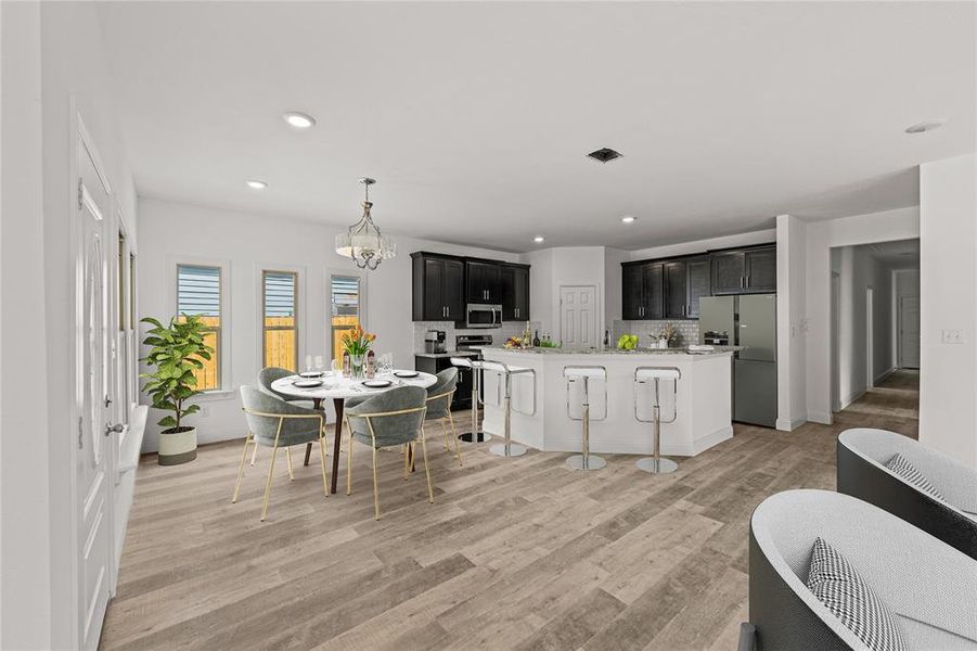 Kitchen featuring a kitchen breakfast bar, tasteful backsplash, stainless steel appliances, a kitchen island with sink, and light hardwood / wood-style flooring