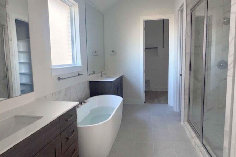 Bathroom with two vanities, a marble finish shower, a freestanding tub, lofted ceiling, and light tile patterned floors