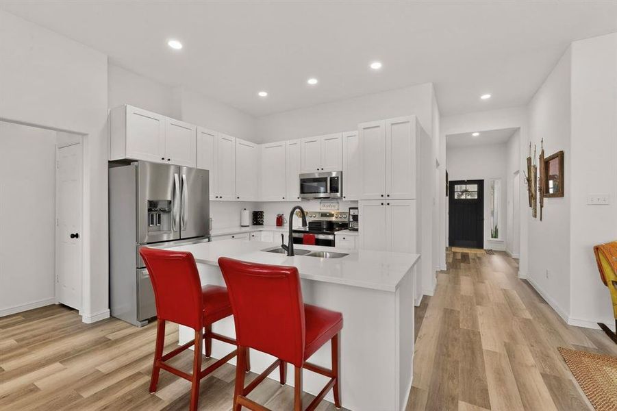 Modern kitchen featuring white shaker cabinetry, stainless steel appliances, a center island with sink, recessed lighting, and wood-finish flooring