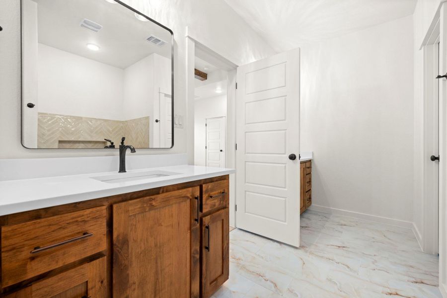 A well-lit bathroom features a rich wood vanity, modern mirror, and elegant marble-look flooring.