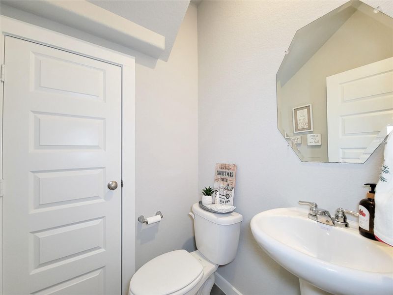 This is a compact, modern bathroom with light-color walls and a sleek design. It features a pedestal sink, a toilet, and a decorative mirror, creating a clean and inviting space. Located on the 1st floor.