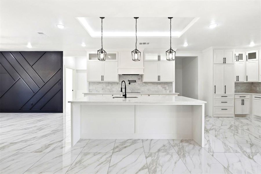 Expansive kitchen featuring a white center island, white cabinetry with black hardware, marble-look tile flooring, and three pendant lights