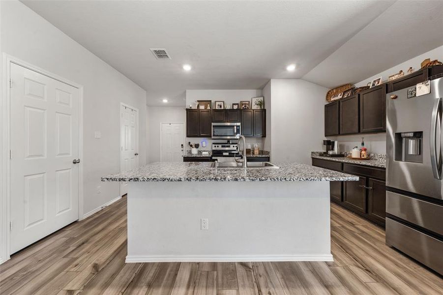 Kitchen featuring appliances with stainless steel finishes, dark brown cabinets, recessed lighting, light wood-style flooring, and a kitchen island with sink
