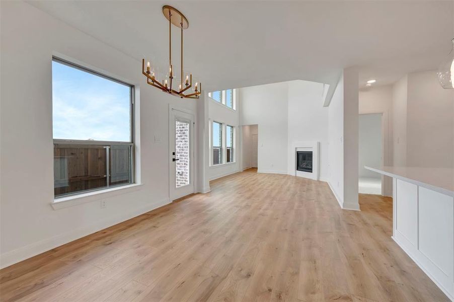 Unfurnished living room featuring a chandelier, light wood finished floors, a glass covered fireplace, and a high ceiling