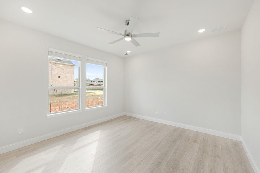 Empty room with light wood floors, white walls, ceiling fan, and two windows with neighborhood view