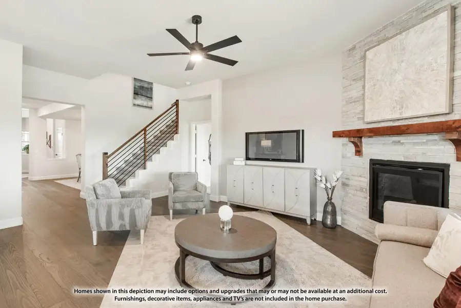 Living room with stone fireplace, ceiling fan, hardwood floors, and staircase with metal railing Living room with stone fireplace, ceiling fan, hardwood floors, and staircase with metal railing
