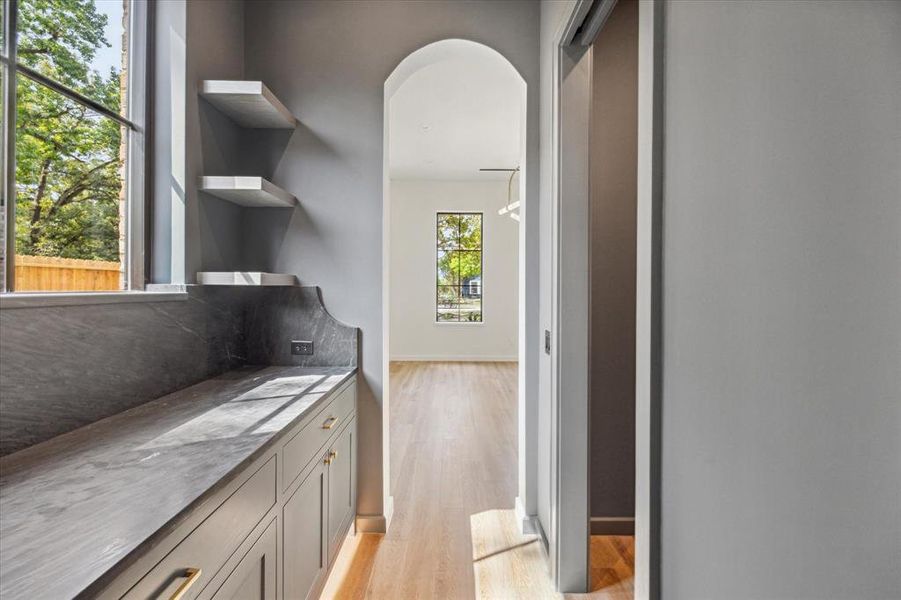 Butlers pantry hallway from kitchen featuring a stone countertop and shelves with full walk-in pantry to the right   and arched doorway leading into formal dining room