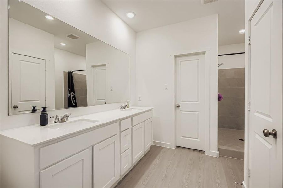 Full bath with a shower stall, double vanity, light wood-style floors, and recessed lighting