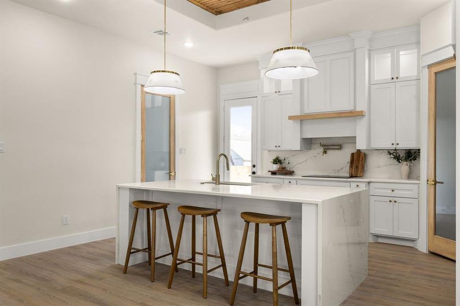 Kitchen featuring tasteful backsplash, baseboards, wood finished floors, a kitchen island with sink, and a sink