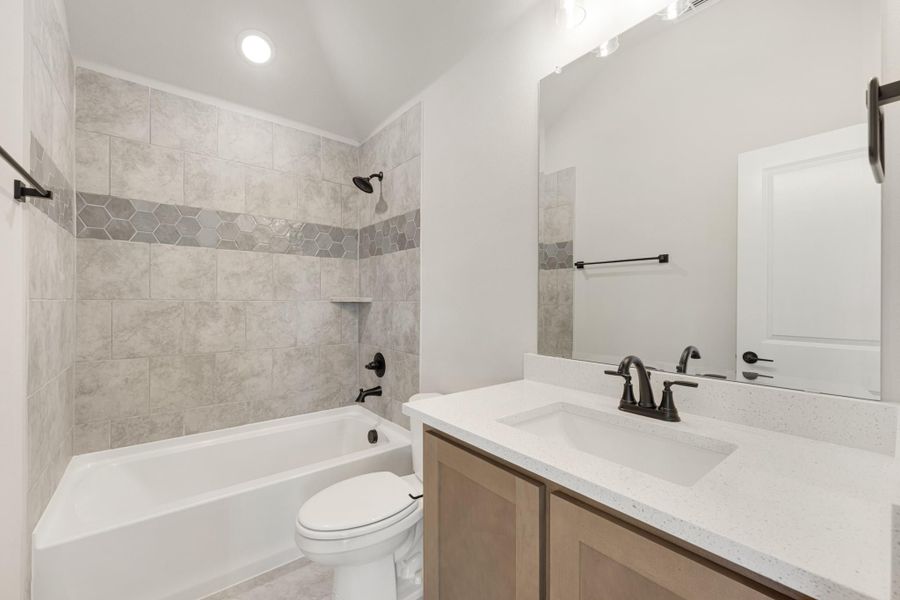 Bathroom with tiled tub-shower combo, wood vanity with white countertop, and large mirror Bathroom with tiled tub-shower combo, wood vanity with white countertop, and large mirror