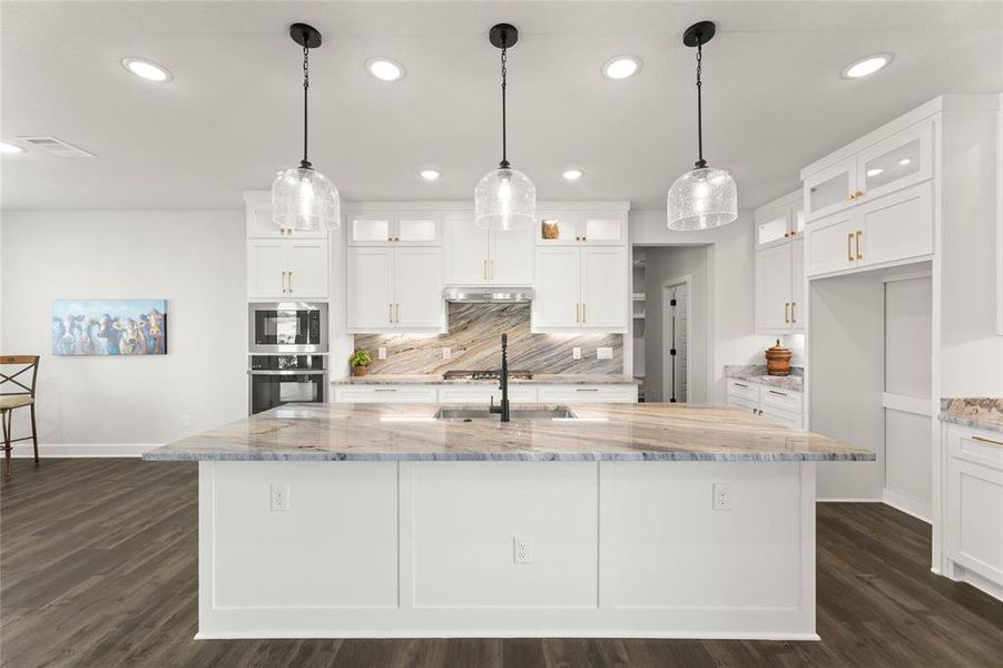 Kitchen with glass insert cabinets, light stone counters, decorative backsplash, recessed lighting, and dark wood-style floors Kitchen with glass insert cabinets, light stone counters, decorative backsplash, recessed lighting, and dark wood-style floors