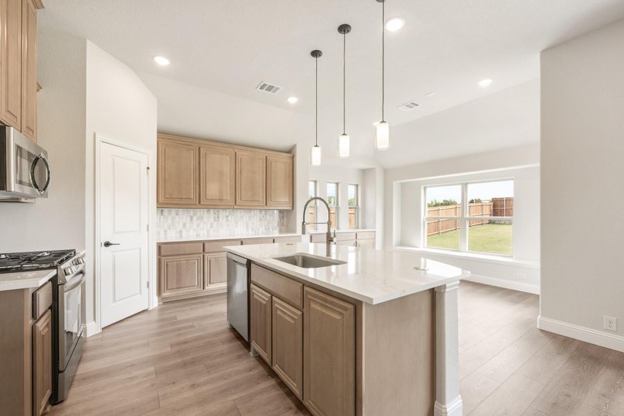 Kitchen with center island, sink, pendant lights, light wood cabinets, and stainless steel appliances on wood-look floors