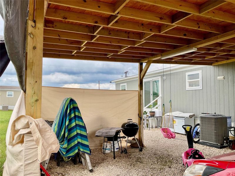 Covered outdoor area featuring a wood-beam ceiling structure, gravel flooring, and privacy screening