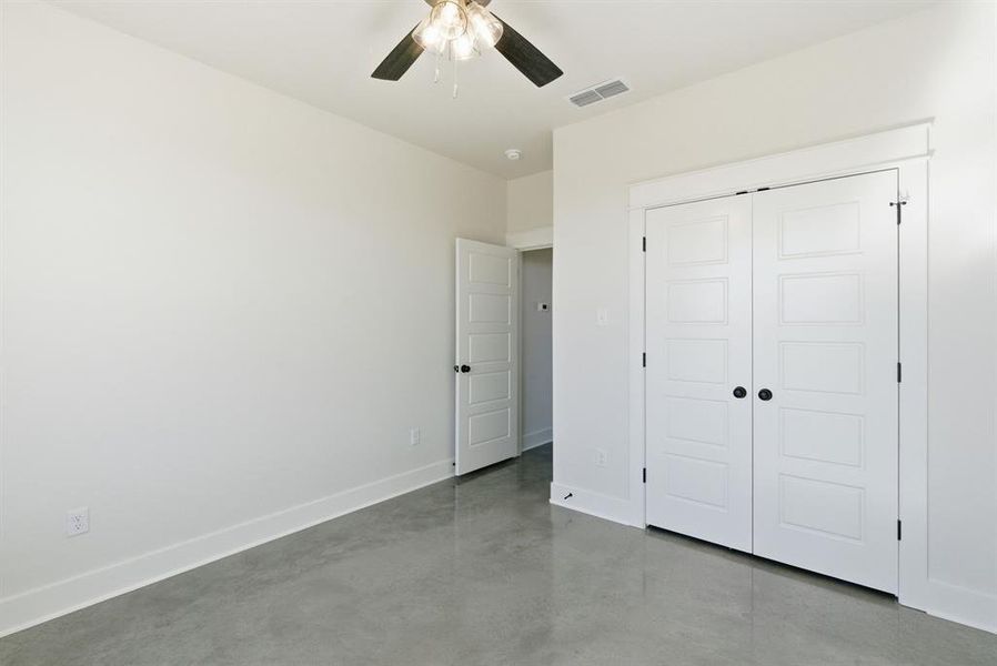 Unfurnished bedroom featuring concrete flooring, ceiling fan, and a closet