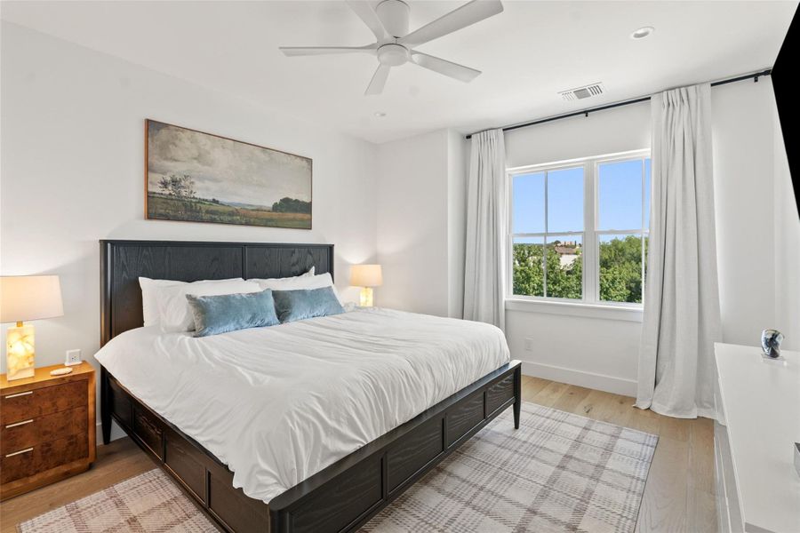 Sun-filled bedroom features light hardwood flooring, a ceiling fan, and a generous window for abundant natural illumination. Sun-filled bedroom features light hardwood flooring, a ceiling fan, and a generous window for abundant natural illumination.