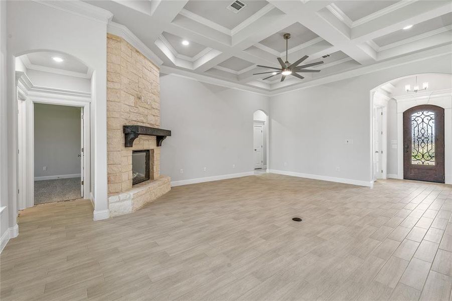 Unfurnished living room featuring arched walkways, light wood-type flooring, crown molding, a stone fireplace, and beam ceiling