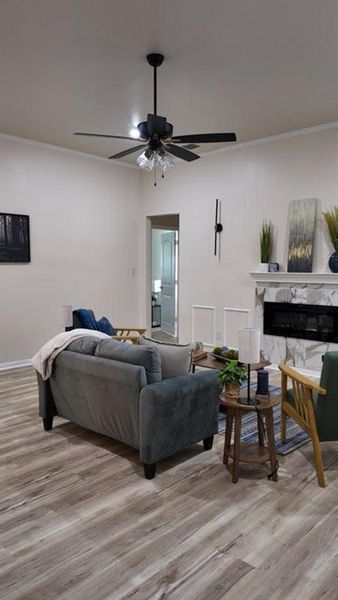Spacious living area featuring wood-finish flooring, a ceiling fan with integrated lighting, and a white stone-faced fireplace with an electric insert