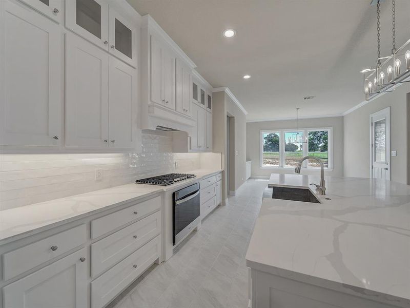 Kitchen with crown molding, white cabinets, pendant lighting, appliances with stainless steel finishes, and light stone countertops Kitchen with crown molding, white cabinets, pendant lighting, appliances with stainless steel finishes, and light stone countertops