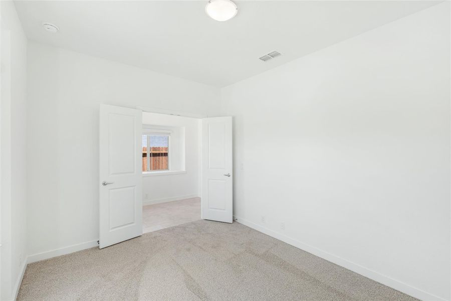 Empty bedroom with white walls, beige carpet, and open double doors leading to another room