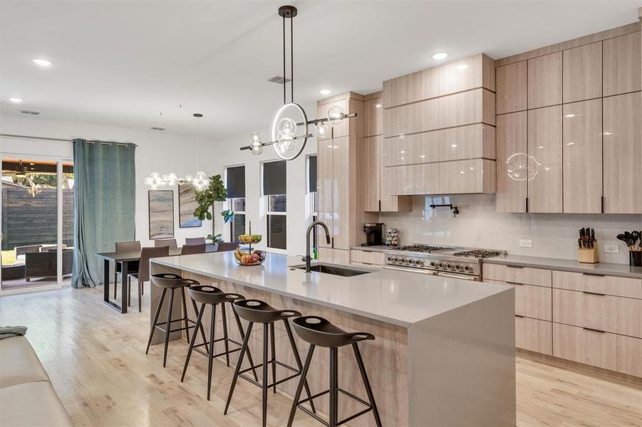 Kitchen featuring sink, a center island with sink, double oven range, and light brown cabinetry