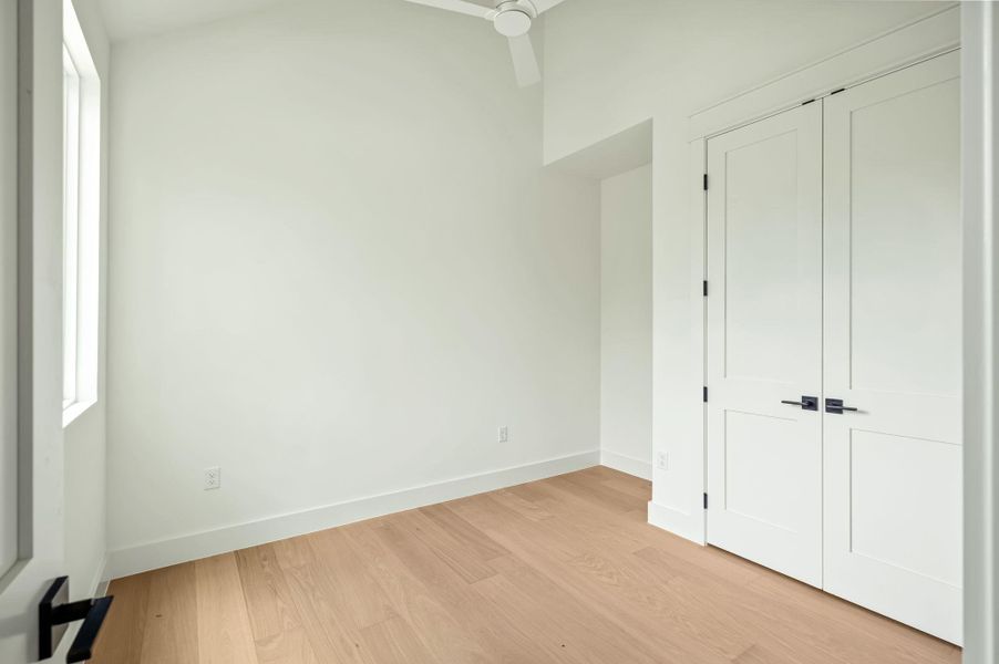 A quiet bedroom featuring light wood flooring and a modern ceiling fan, offering a serene retreat.