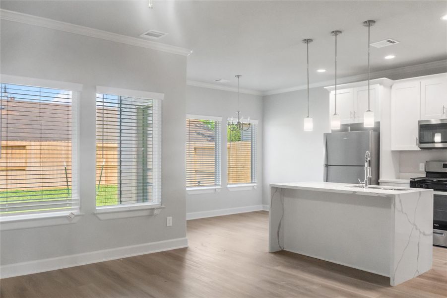 This photo showcases a modern, open-concept kitchen and dining area with abundant natural light. It features sleek stainless steel appliances, a large island with a marble countertop, pendant lighting, and light wood flooring, creating a bright and inviting space.
