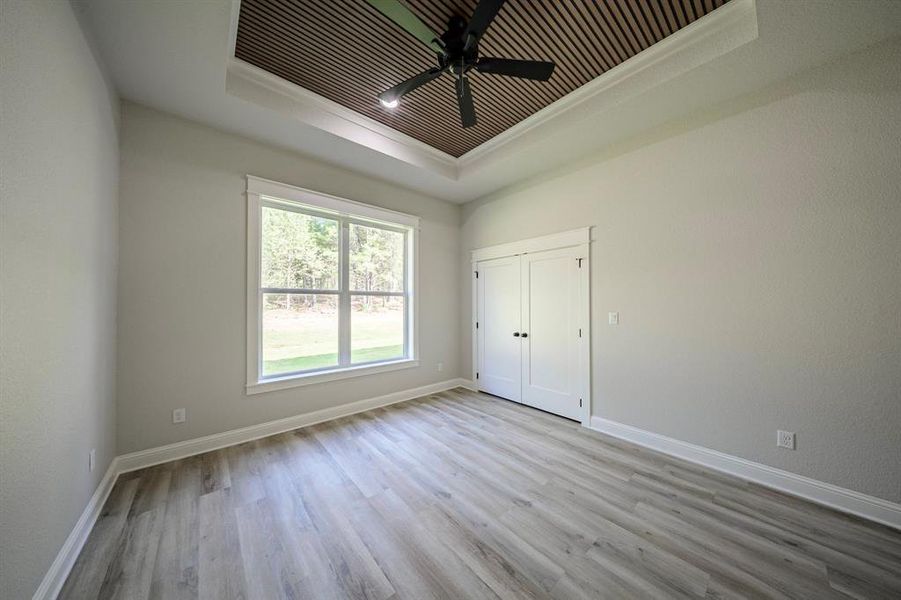 Unfurnished bedroom featuring a raised ceiling, light wood-style flooring, ceiling fan, and a closet Unfurnished bedroom featuring a raised ceiling, light wood-style flooring, ceiling fan, and a closet