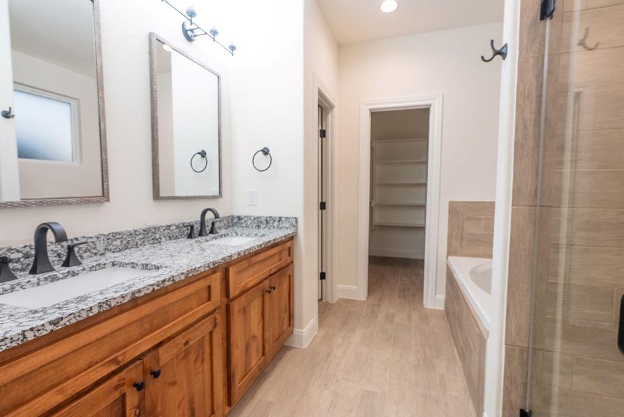 Full bath with double vanity, a bath, light wood finished floors, a spacious closet, and a shower stall Full bath with double vanity, a bath, light wood finished floors, a spacious closet, and a shower stall