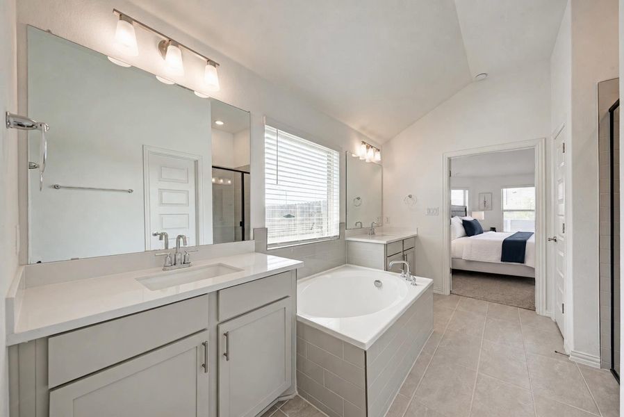 A bright primary bathroom with dual vanities and a deep soaking tub, offering serene access to the bedroom.