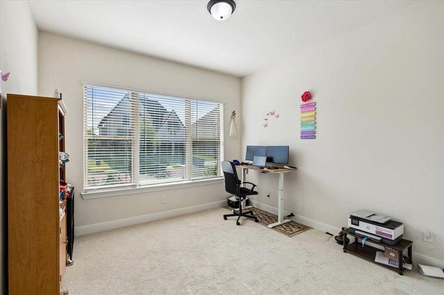 Bright room featuring a large window with horizontal blinds, neutral wall tones, and light-colored carpeting Bright room featuring a large window with horizontal blinds, neutral wall tones, and light-colored carpeting