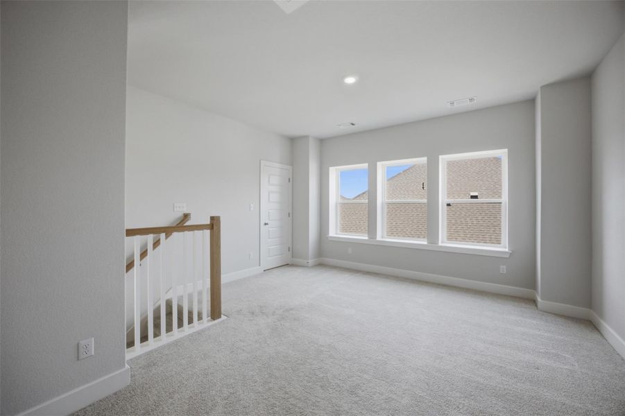 A spacious secondary living area features soft carpeting and ample natural light through three bright windows.