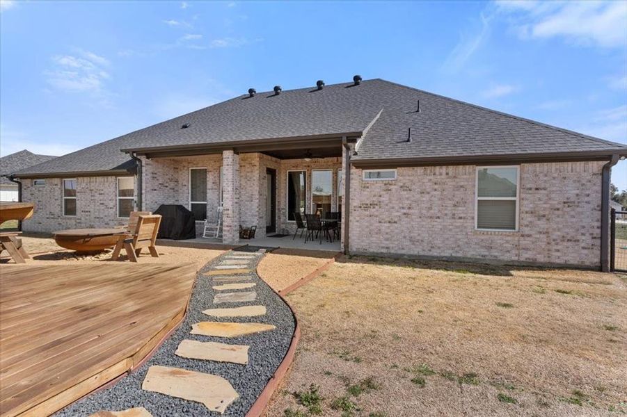 Back of house featuring brick siding, a shingled roof, a deck, and a patio