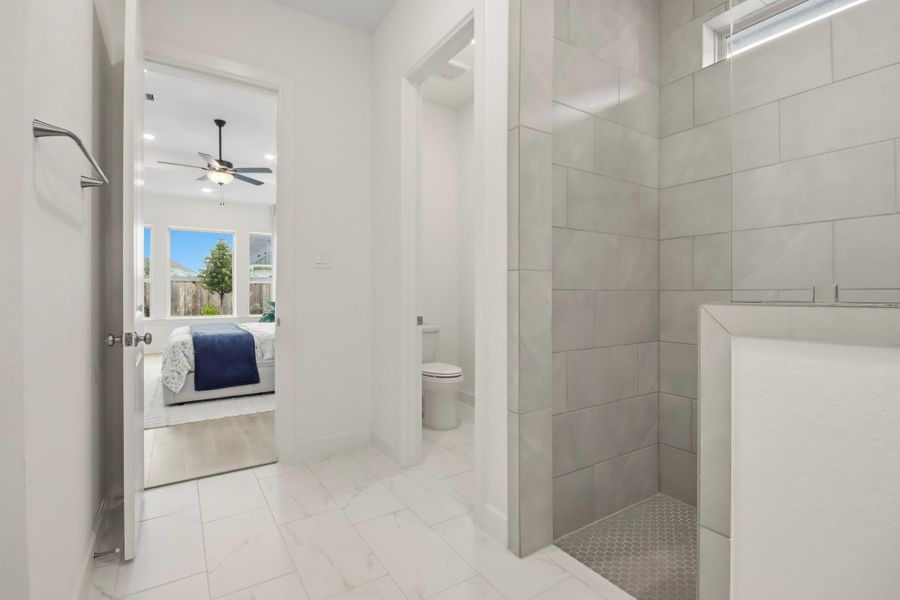 Contemporary bathroom featuring a beautifully tiled shower and seamless access to a bright bedroom with oversized windows and a ceiling fan.