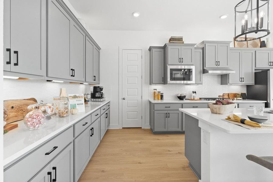 Kitchen featuring gray cabinetry, light wood-style flooring, light stone countertops, stainless steel appliances, and a chandelier