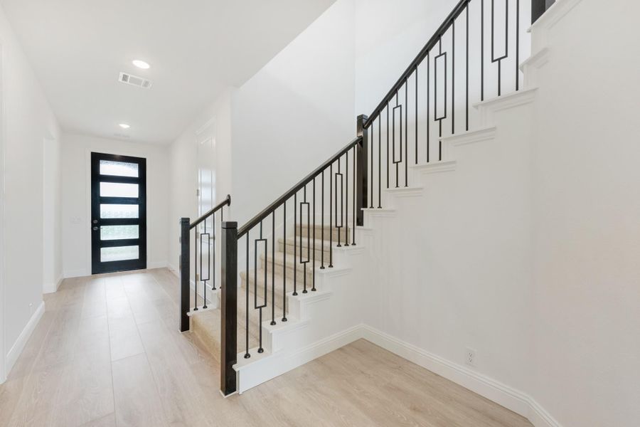 Bright entryway with staircase featuring black metal railing, light wood floors, and glass-panel front door Bright entryway with staircase featuring black metal railing, light wood floors, and glass-panel front door