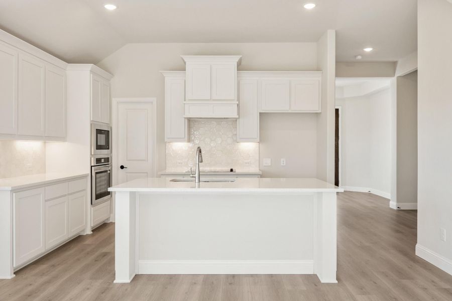 White kitchen with large center island, white cabinets, tile backsplash, and light hardwood floors